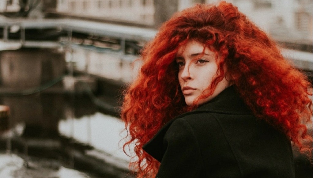 Vrouw met rode krullen kijkt in de verte