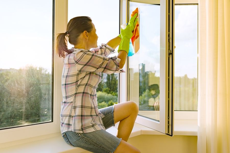 Jonge vrouw wast de ramen met milieuvriendelijke schoonmaakmiddelen