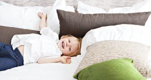Klein jongetje speelt in het bed van zijn ouders omringd door sierkussens