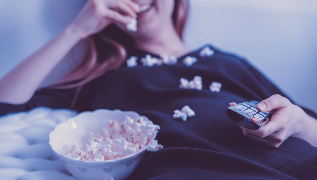 Vrouw kijkt film met popcorn op de bank