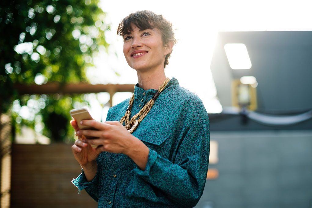 Vrouw in blauwe bloes kijkt op van haar mobiel, met haar mobiel nog in haar handen