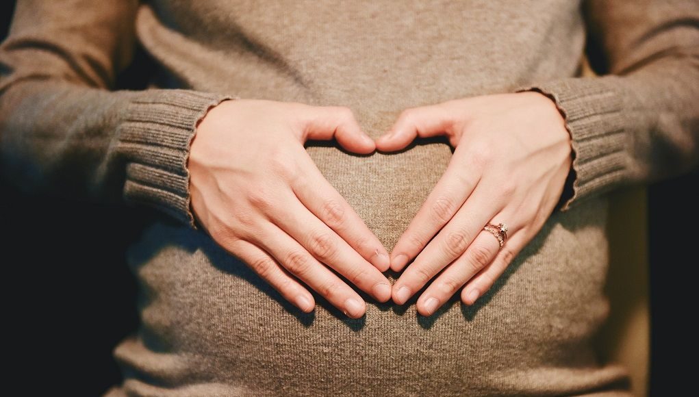 Vrouw houdt haar zwangere buik vast, handen in de vorm van een hart
