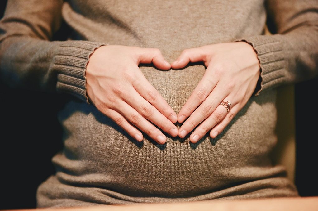 Vrouw houdt haar zwangere buik vast, handen in de vorm van een hart