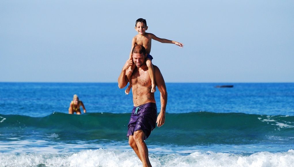 Betrokken vader op een surfboard met zijn zoontje op zijn nek