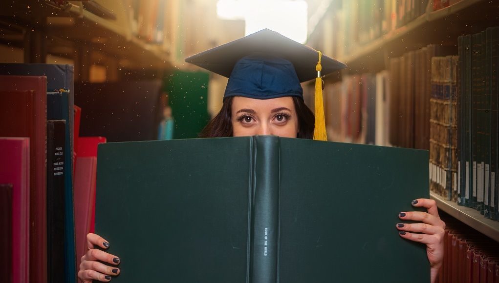 Vrouw met universitaire hoed verstopt zich achter boek
