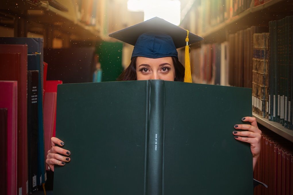 Vrouw met universitaire hoed verstopt zich achter boek