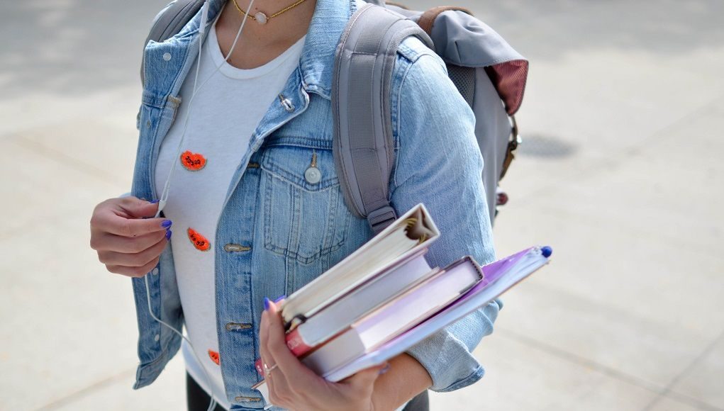 Meisje met schoolboeken op haar arm en rugzak