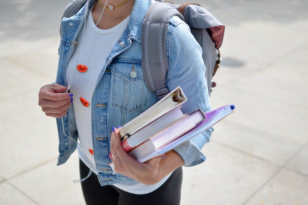 Meisje met schoolboeken op haar arm en rugzak
